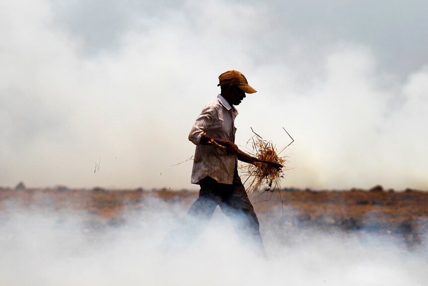 Un agriculteur marche dans la fumée en transportant de l'herbe séchée et des brindilles à brûler dans son champ.