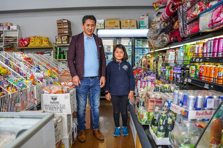 A man and young girl in a school uniform stand in the middle of a grocer aisle smiling.