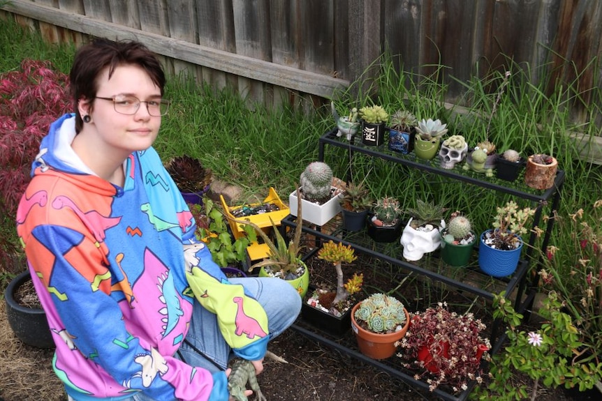 A young man outside wearing a colourful hoodie and glasses smiles