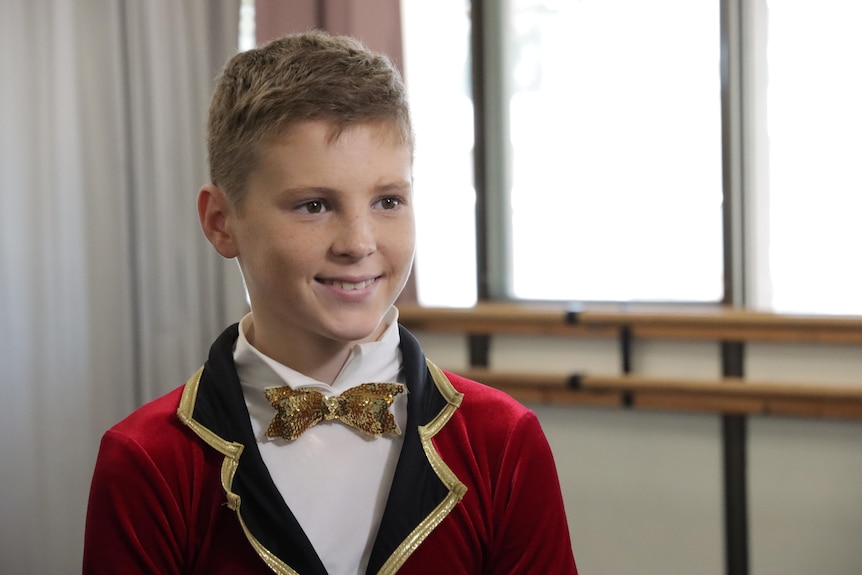 A photo of Tyce Smith in his stage uniform which is red black jacket and a gold bow tie smiling at the camera