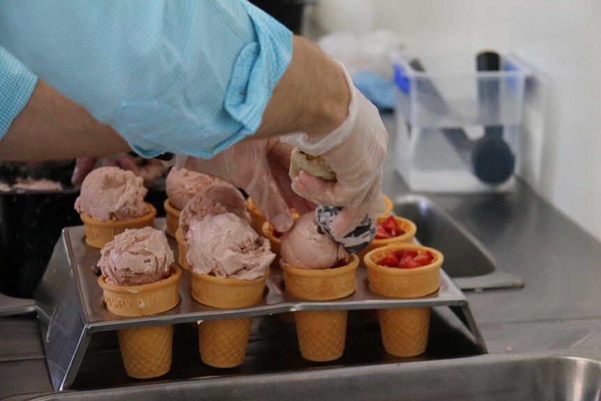 Adding the strawberry ice cream to the strawberry sundaes