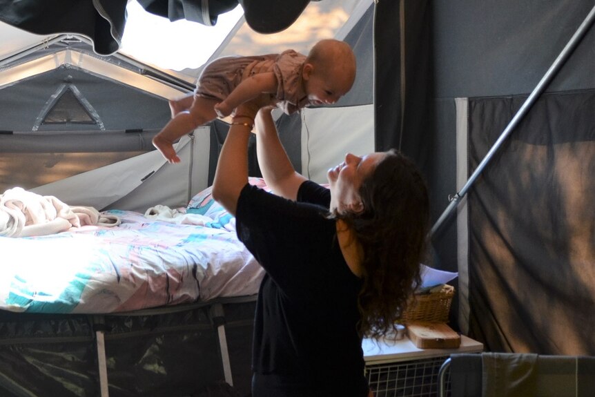 A mother holds her baby aloft both smiling, inside a tent