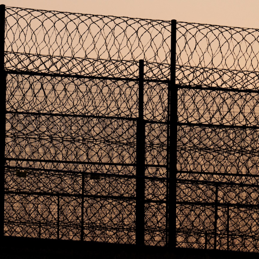 Barbed wire and a high fence pictured against a sunset
