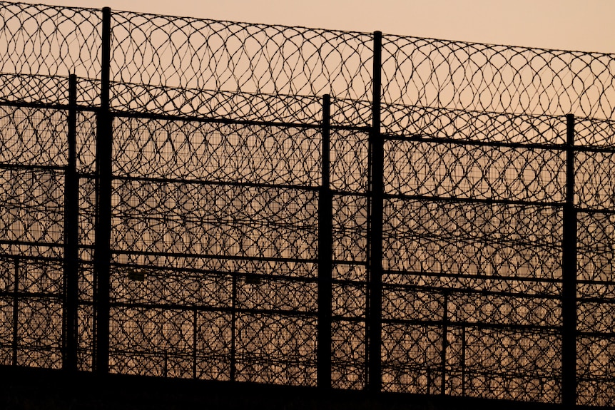 Barbed wire and a high fence pictured against a sunset