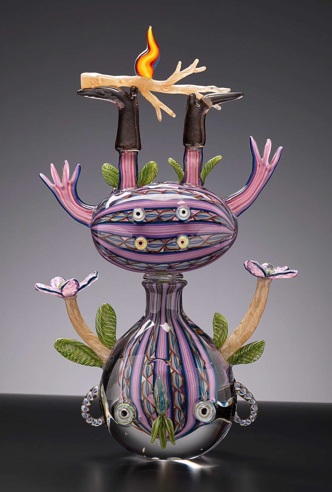 A glass character by Tom Moore - an upside down figure in intricate, multicoloured tones 