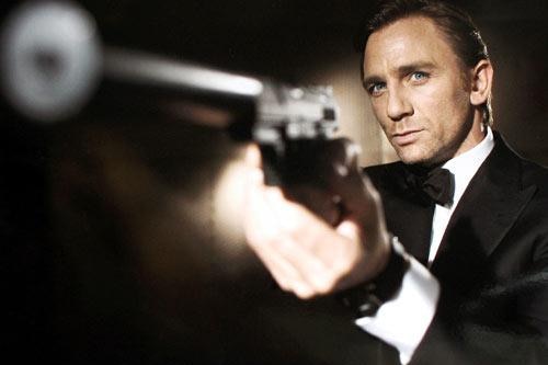 Holding a long-nozzle, out-of-focus pistol, an in-focus, serious Daniel Craig takes aim in a publicity shot