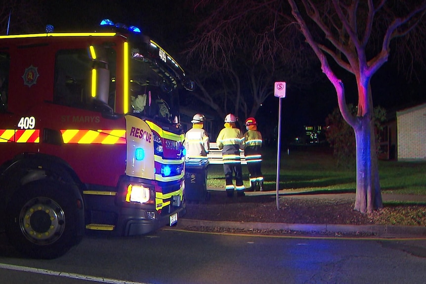 Three firefighters stand next to a fire truck in the dark