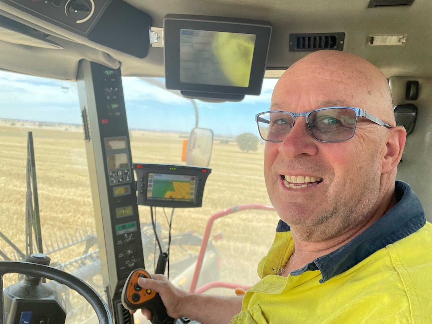 A man sitting in a header stripping a crop smiling.