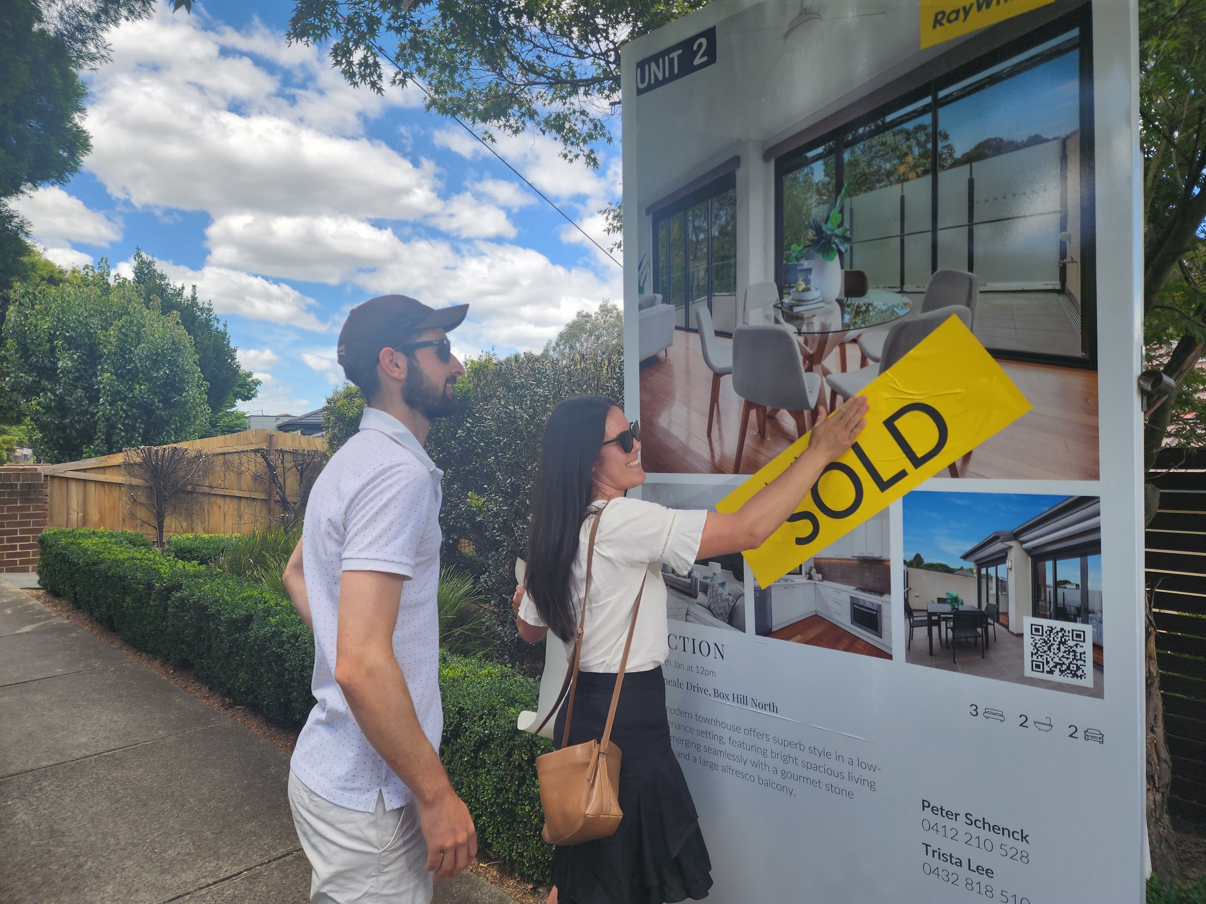 young couple put sold sticker on billboard of their newly purchased home.