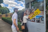 young couple put sold sticker on billboard of their newly purchased home.