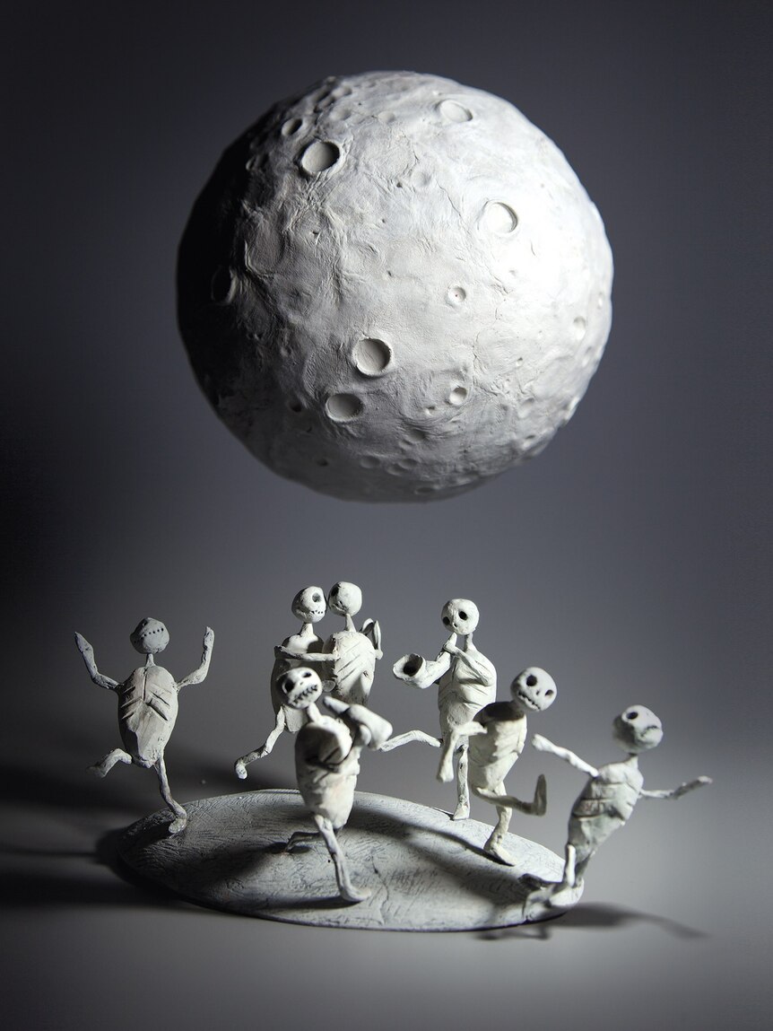 Small human-like figurines under a moon-like shape.