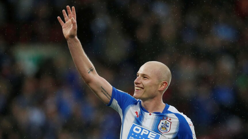 Aaron Mooy raises his hand to the crowd and smiles.