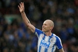 Aaron Mooy raises his hand to the crowd and smiles.