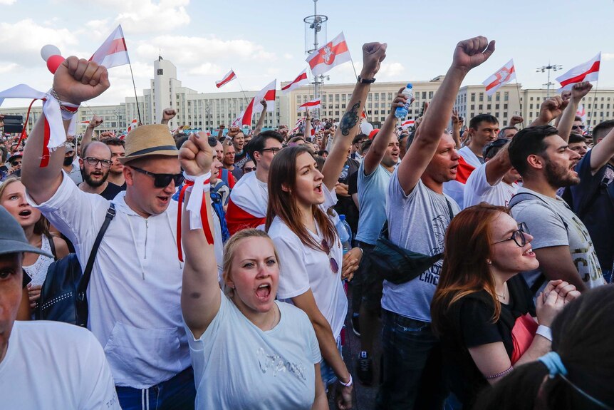People with old Belarusian flags hold up their fists in protest against the re-election of President Alexander Lukashenko.