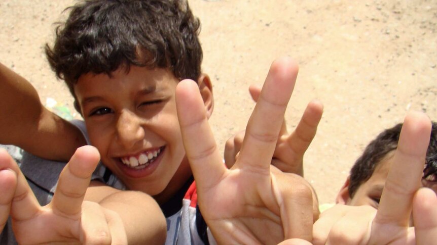 Children hold two fingers up in a victory symbol in a desert setting.