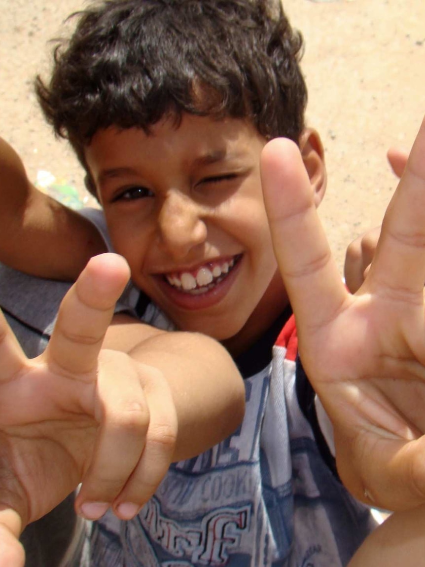 Children hold two fingers up in a victory symbol in a desert setting.