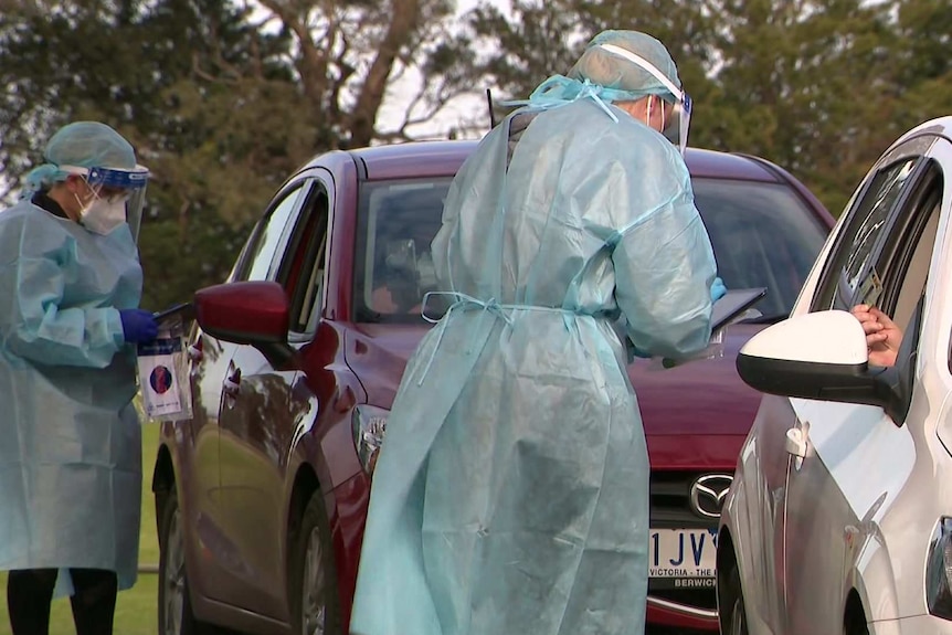 Two medical workers in PPE test two drivers for COVD-19.