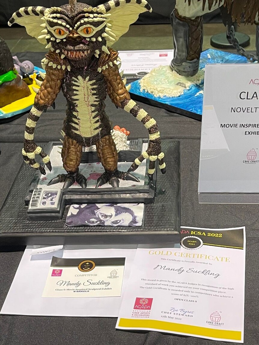 A gremlin cake on a table with certificates underneath it
