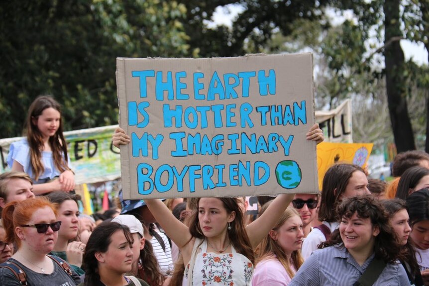 A teenage girl holds a sign that says: 'The earth is hotter than my imaginary boyfriend'.