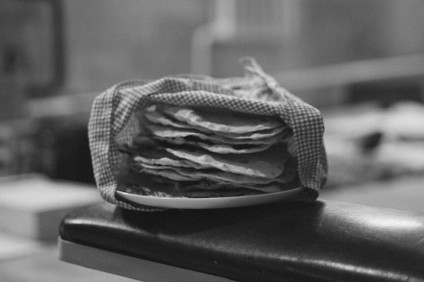A stack of flatbreads under a cloth in black and white.