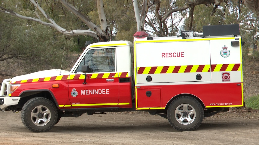 A red Rural Fire Service rescue vehicle, parked on dirt, surrounded by trees. 