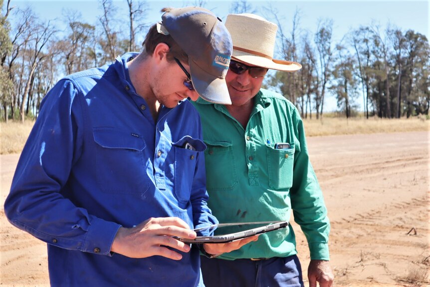 Tom and Phillip Coggan stand in a paddock and use their iPad to operate a Spray Bot.