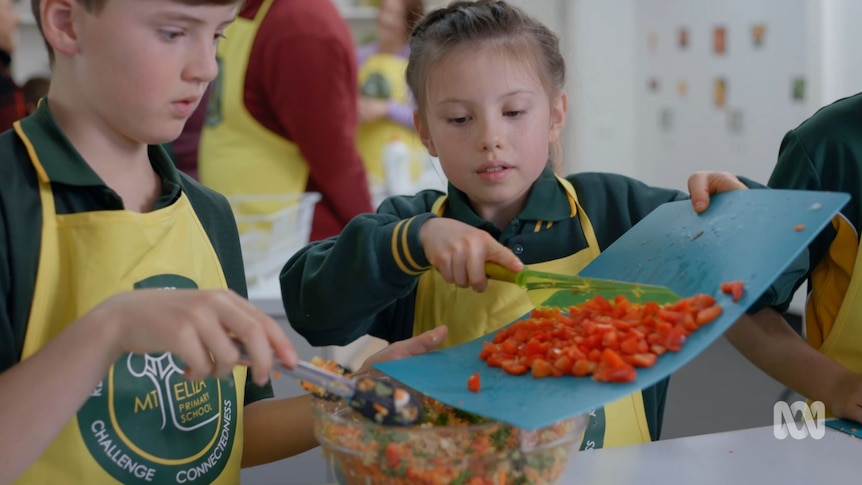 Students top chopped vegetables into a bowl