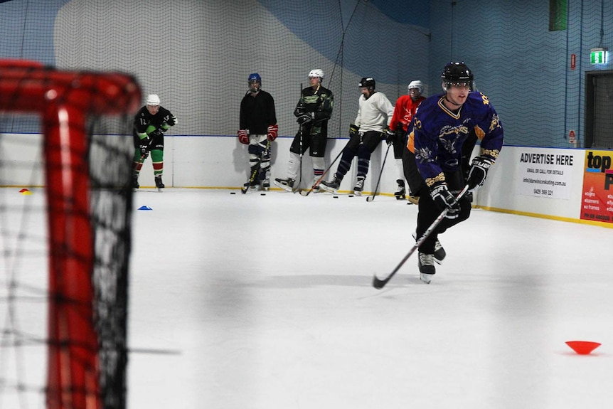 A man approaches the goal on an ice-skating rink, gearing up to take a shot.