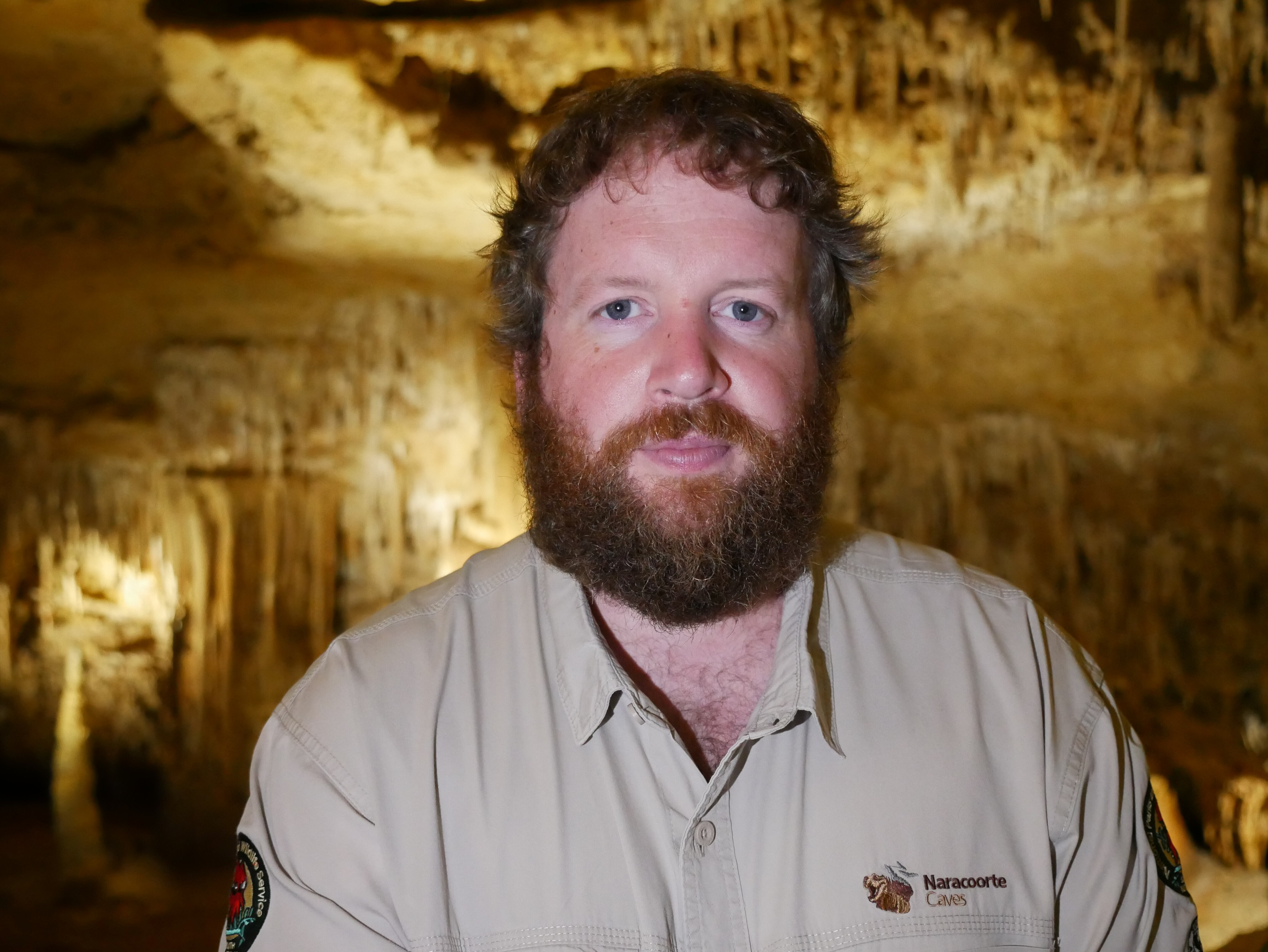 A man wearing a green shirt standing in a cave. 