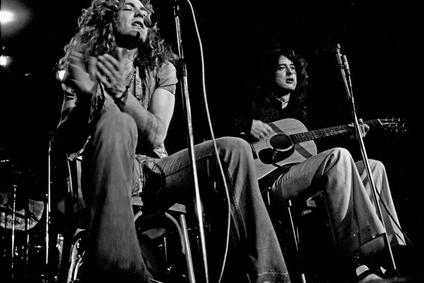 Close up intimate black and white photograph of robert plant and jimmy page with long flowing 70s hair playing acoustic