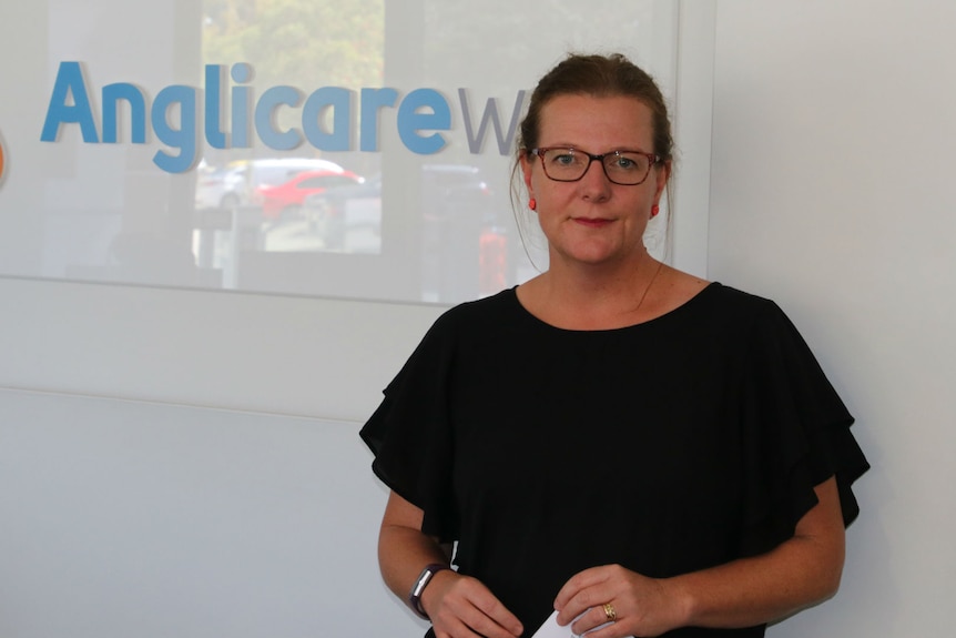 Philippa Boldy stands in front of Anglicare logo on wall