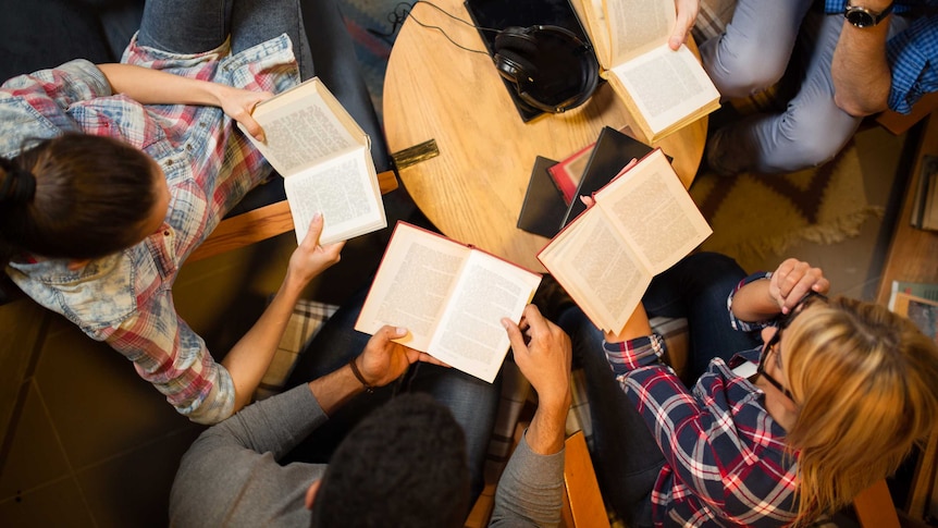 An overhead shot of four young people reading at a small table.