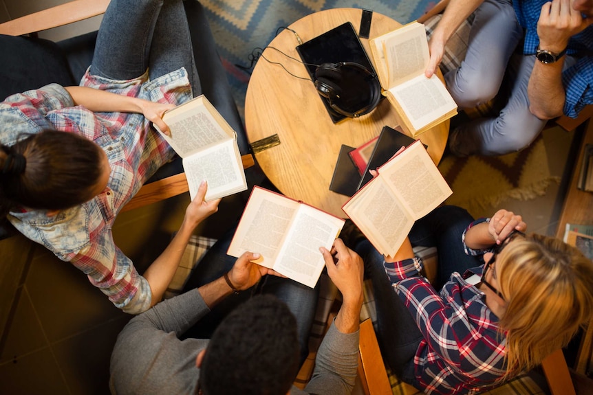 An overhead shot of four young people reading at a small table.