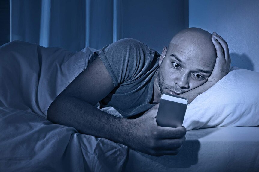 A man looks at his phone in bed