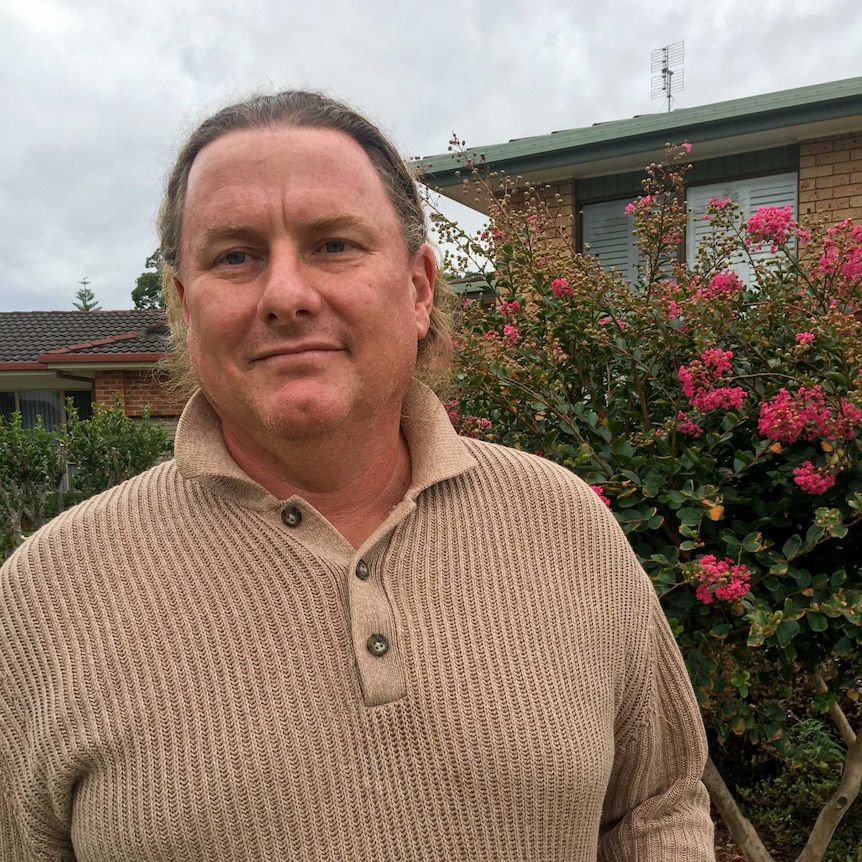 Sean Ladlow standing in his garden wearing a brown jumper, smiling.