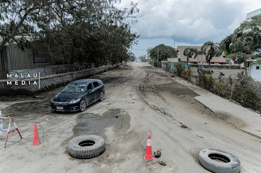 Ash covered road blocked off by orange cones and tyres after Tonga's volcanic eruption. 