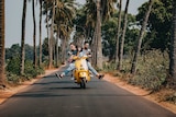 Smiling man and woman riding on scooter on a narrow road for a story about the challenges and joys of travelling with family.