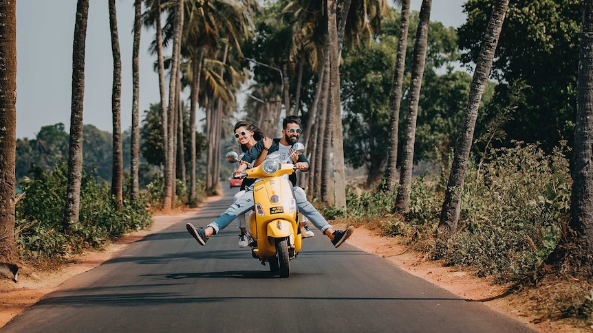 Smiling man and woman riding on scooter on a narrow road for a story about the challenges and joys of travelling with family.