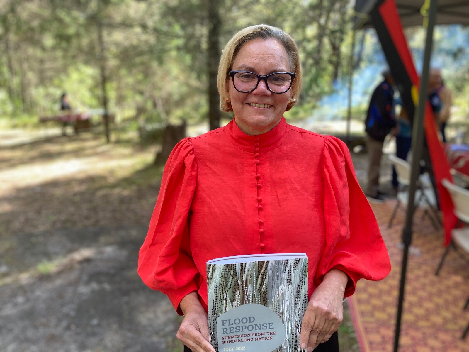 Woman in red top and black glasses holds a report