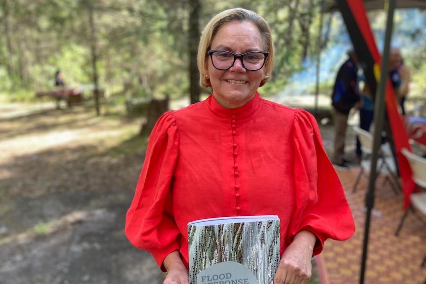 Woman in red top and black glasses holds a report