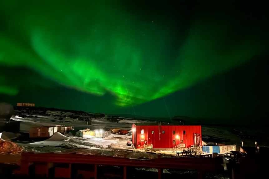 A red building lit up at night, beneath a green coloured aurora Australis (southern lights)