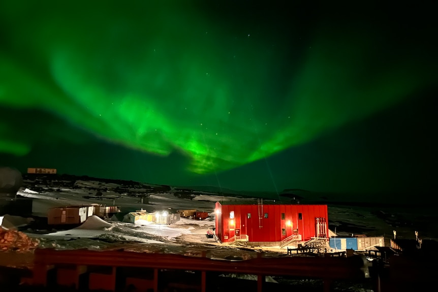 A red building lit up at night, beneath a green coloured aurora Australis (southern lights)