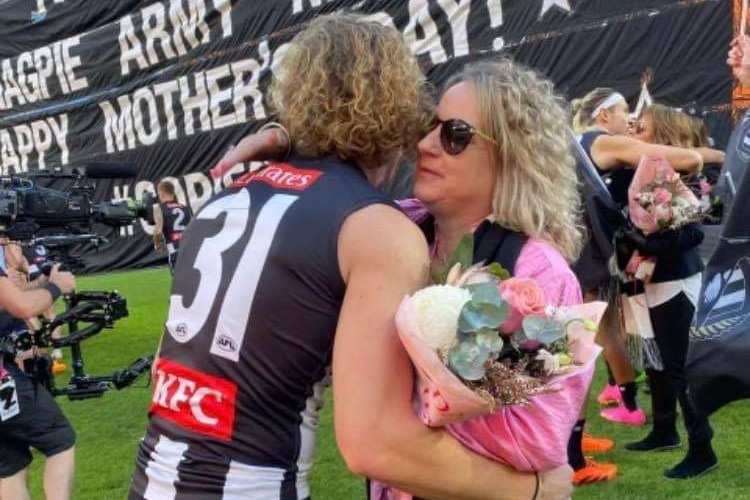 Beau McCreery hugs his mum on the oval with a mother's day banner in the background