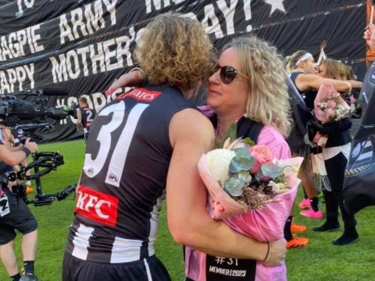 Beau McCreery hugs his mum on the oval with a mother's day banner in the background