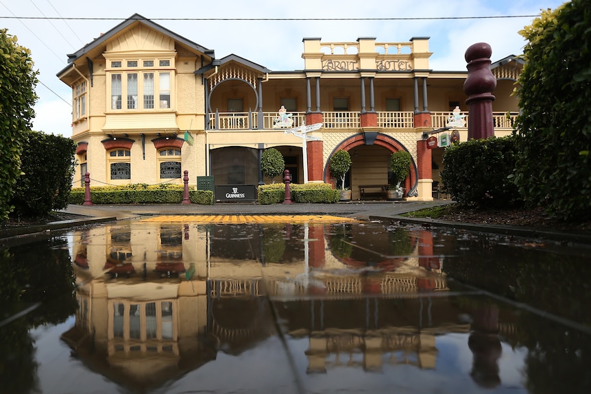 Exterior of old pub reflected in pond across the street. Sign says Koroit Hotel. 