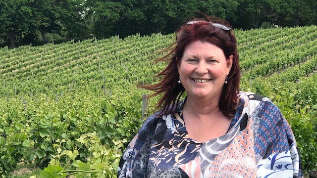 Natalie Fryar stands in front of vineyard.