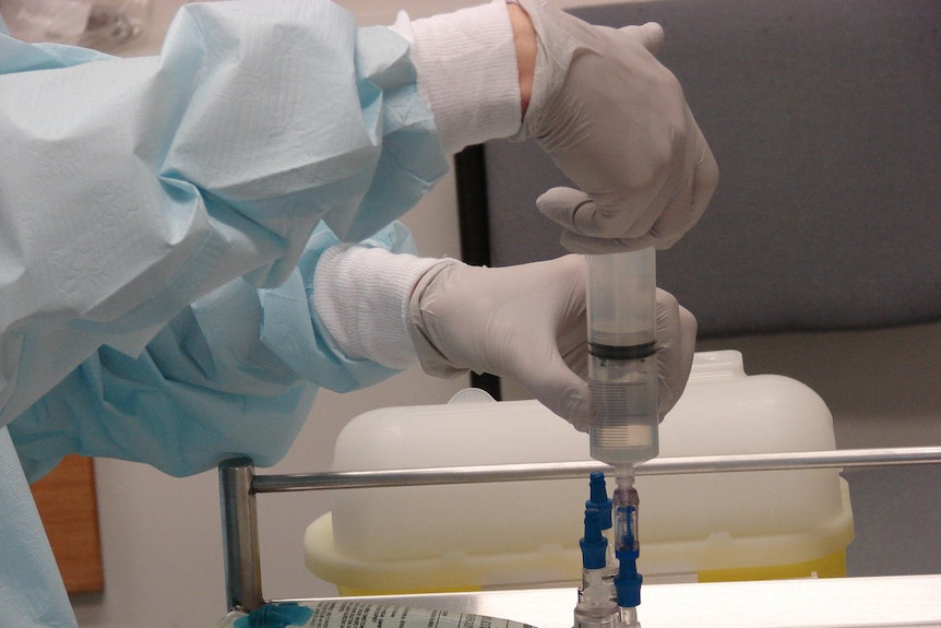 A doctor wearing gloves prepares a saline drip.