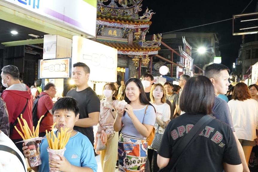 Kid walks with chips and crowds in street.