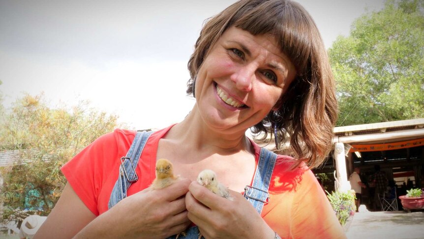 A smiling woman holds two small chicks