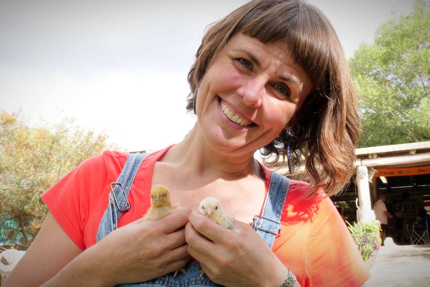 A smiling woman holds two small chicks